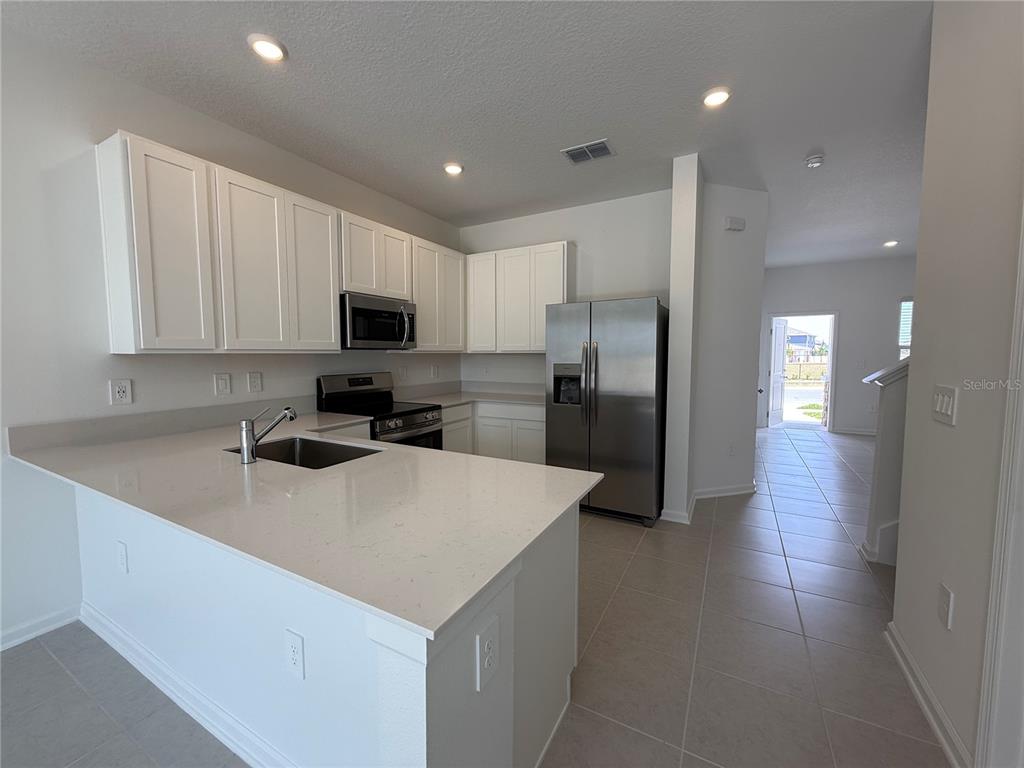 A kitchen features white cabinets, stainless steel appliances, and a quartz-topped island with a sink — 2945 PROSPERITY WAY, CLERMONT, FL