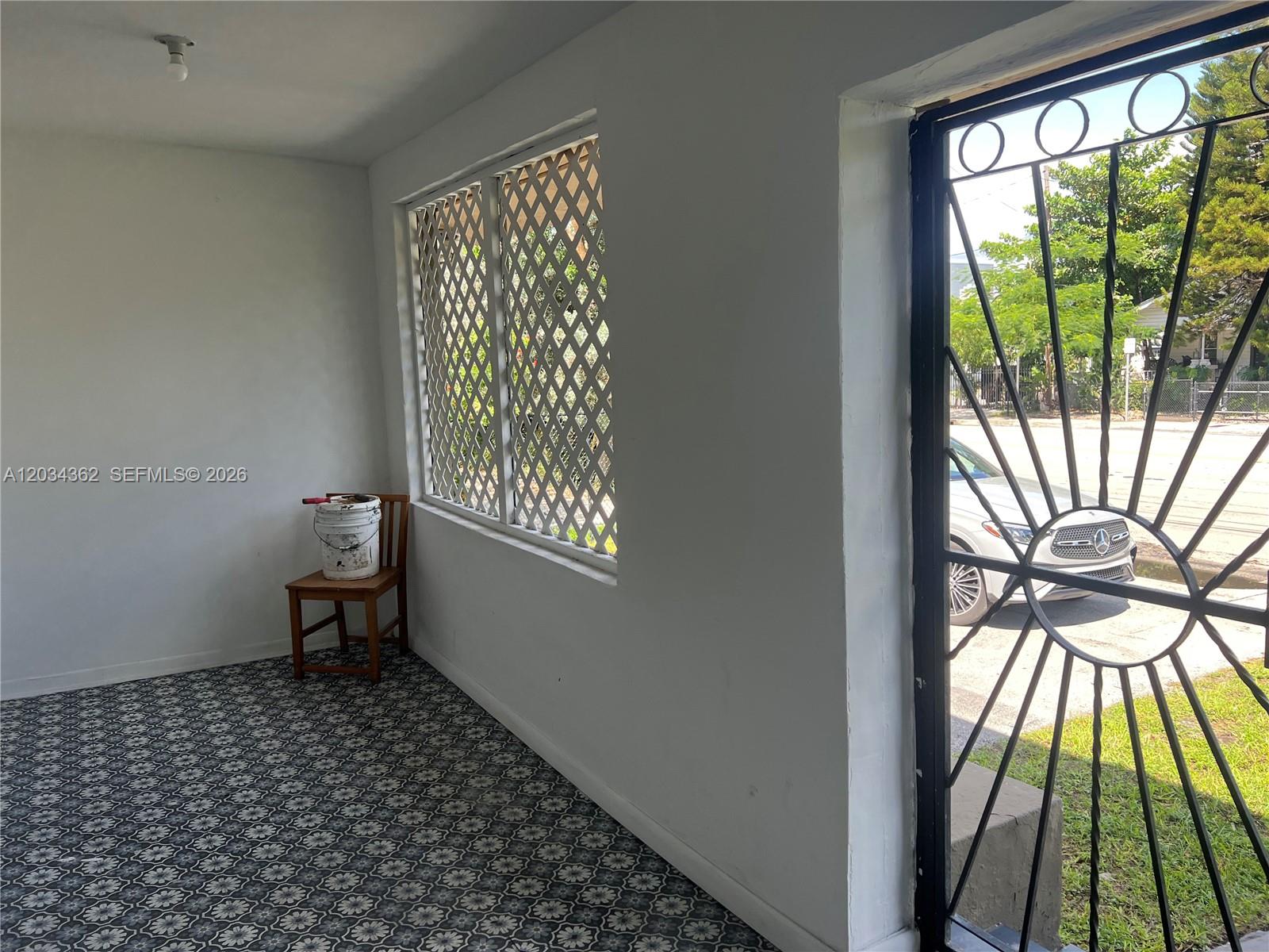A sunroom features patterned tile flooring, a wooden chair with a bucket, and a security gate — 842 SW 12th Ave, Miami FL 33130, MIAMI, FL