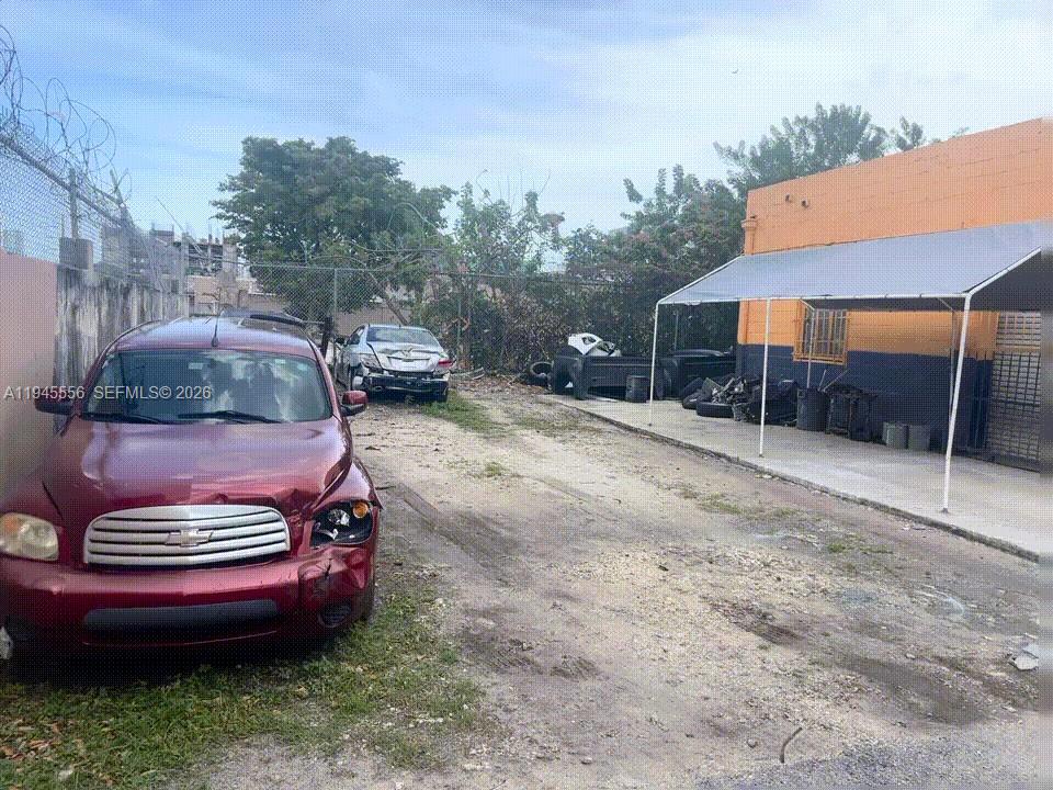 A damaged red car sits on a gravel lot next to an orange building — 2005 NW 10th Ave, Miami FL 33127, MIAMI, FL