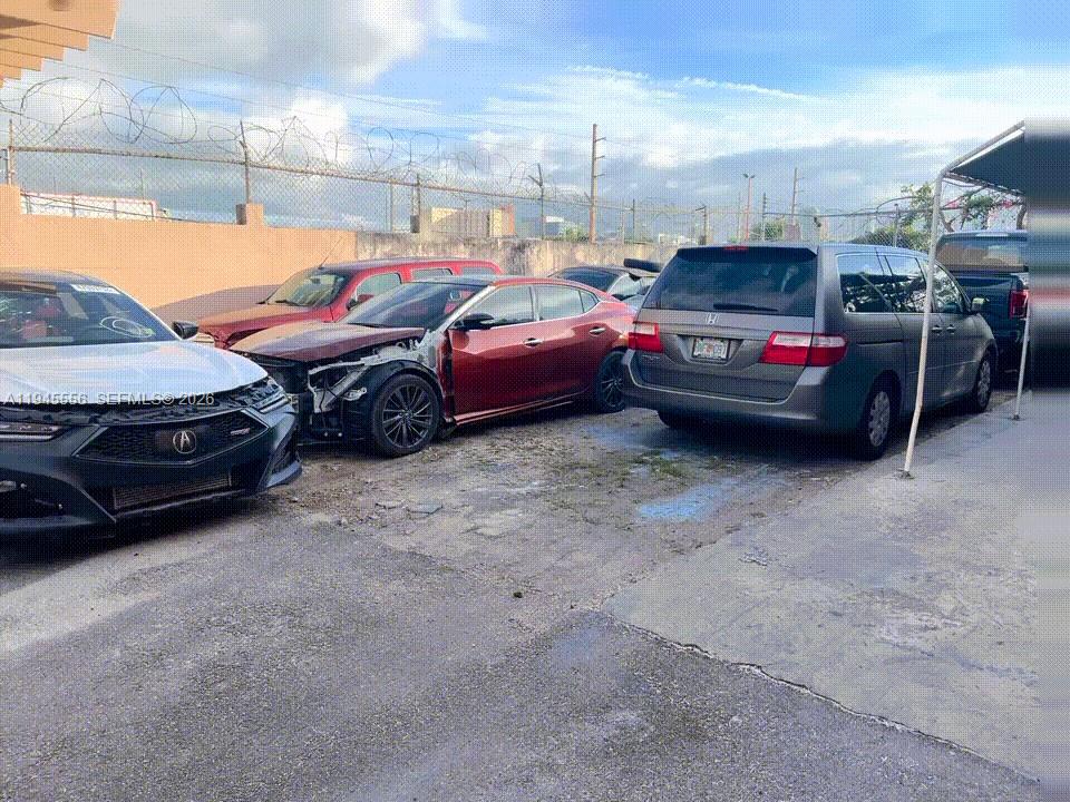 Several damaged vehicles are parked in a fenced outdoor lot under a cloudy sky — 2005 NW 10th Ave, Miami FL 33127, MIAMI, FL