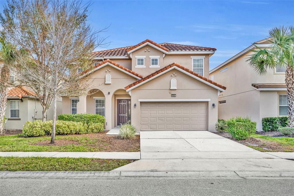 A two-story suburban house with a tan stucco exterior, tile roof, and attached two-car garage — 5244 OAKBOURNE AVENUE, DAVENPORT, FL