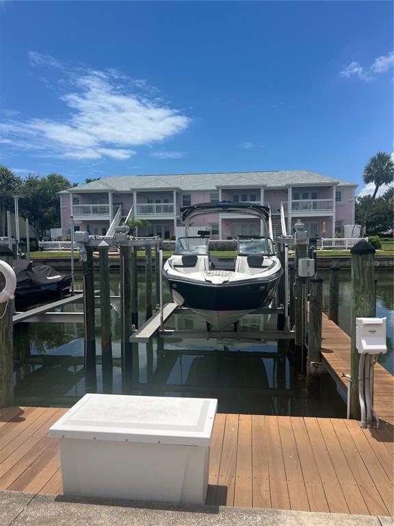 A boat sits on a lift in a canal in front of a pink building — 00 COQUINA KEY DRIVE SE UNIT 107SS, ST PETERSBURG, FL