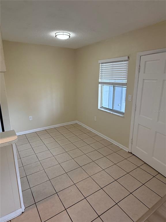 A small, empty dining area features beige tile flooring, a window with blinds, and a door — 2099 KINGS HWY #1 UNIT 1, CLEARWATER, FL
