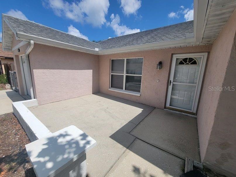 A pink stucco house exterior features a concrete patio, a window, and a white door — 8224 AUTUMN OAK AVENUE, PORT RICHEY, FL