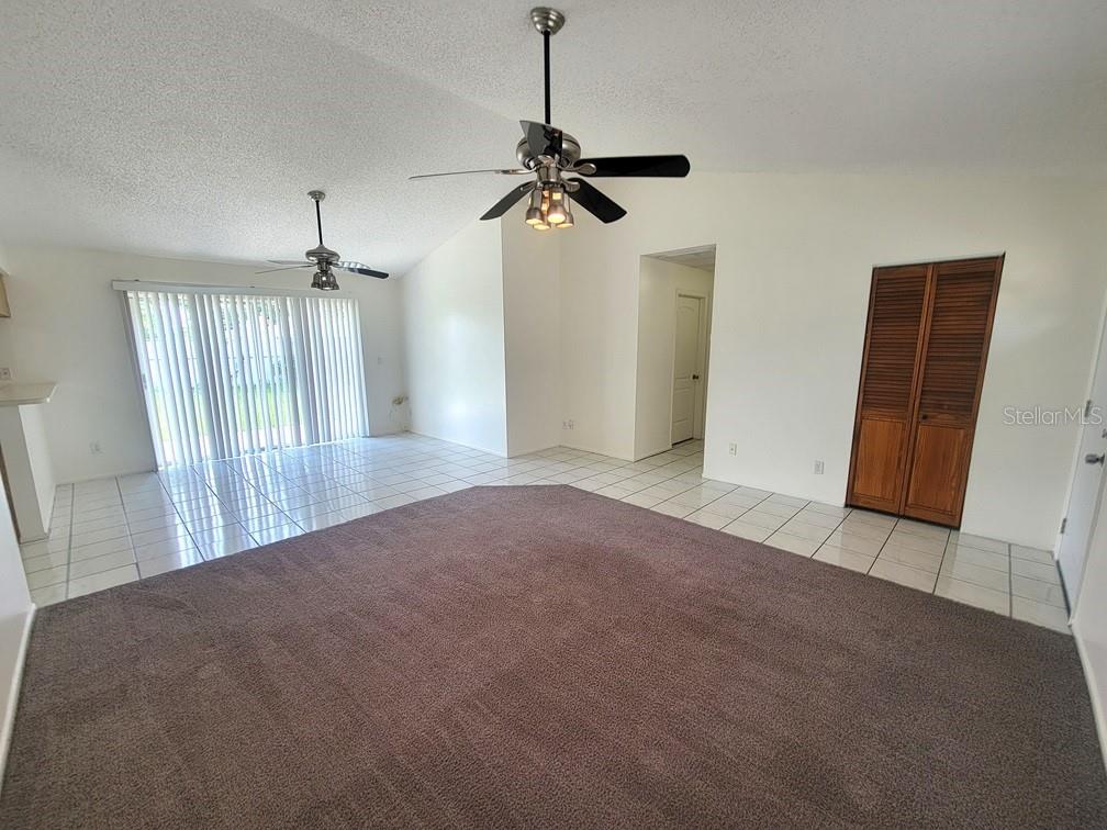 A living room features brown carpeting, white tile flooring, two ceiling fans, and sliding doors — 8224 AUTUMN OAK AVENUE, PORT RICHEY, FL