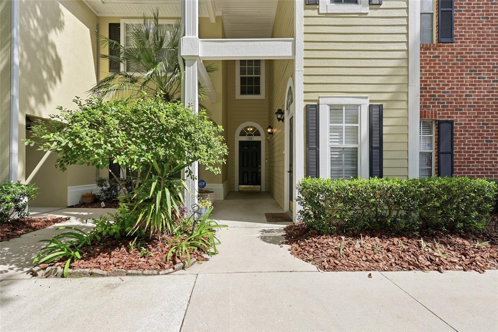 The exterior of a two-story townhouse features a covered entryway, light siding, and brick accents — 10000 SW 52ND AVENUE UNIT 71, GAINESVILLE, FL