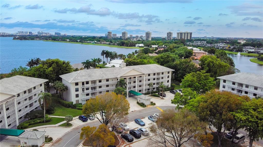 An aerial view shows multi-story apartment buildings surrounded by trees, parking lots, and a lake — 3635 WHITEHALL DRIVE UNIT 401, WEST PALM BEACH, FL