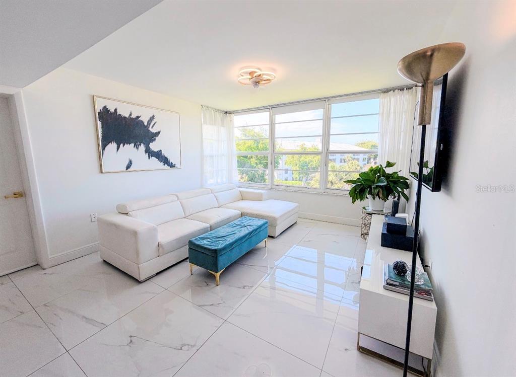 A living room features a white sectional sofa, blue ottoman, and large windows with views — 3635 WHITEHALL DRIVE UNIT 401, WEST PALM BEACH, FL