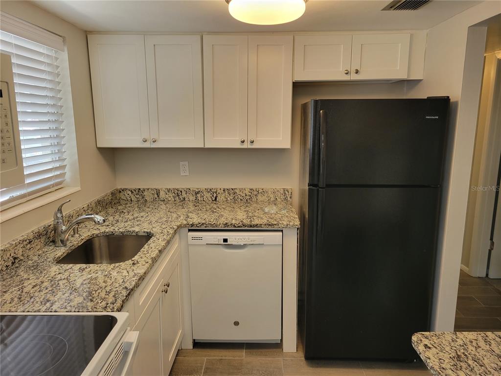 A kitchen features white cabinets, granite countertops, a stainless steel sink, and black appliances — 2009 CANAL DRIVE UNIT N4, BRADENTON, FL