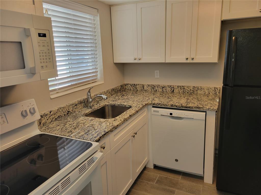 A kitchen features white cabinets, granite countertops, a stainless steel sink, and white appliances — 2009 CANAL DRIVE UNIT N4, BRADENTON, FL