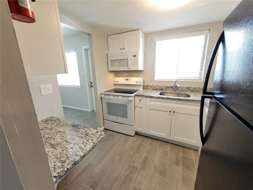 A kitchen features white cabinets, granite countertops, a black refrigerator, and gray wood-look flooring — 2009 CANAL DRIVE UNIT N4, BRADENTON, FL
