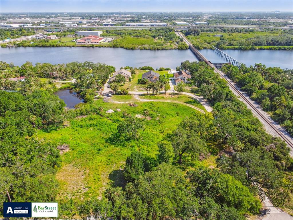 An aerial view shows a large grassy lot with three houses near a river and tracks — 5116 PALM RIVER ROAD, TAMPA, FL
