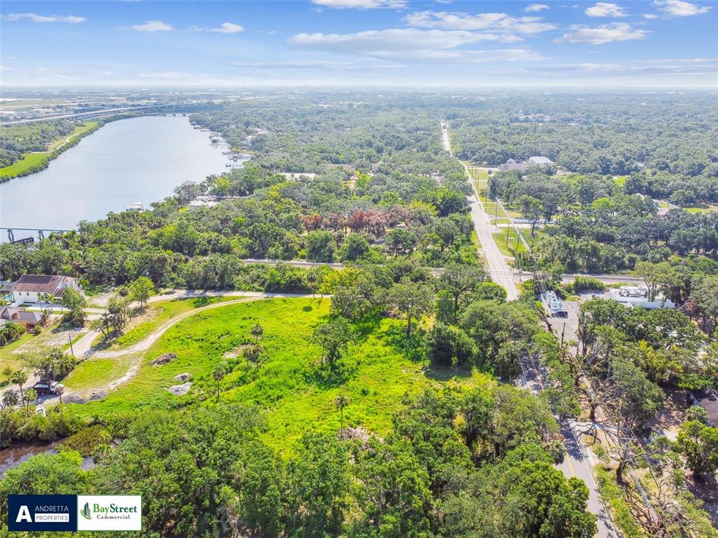 An aerial view shows a grassy lot bordered by a road, trees, and a river — 5116 PALM RIVER ROAD, TAMPA, FL