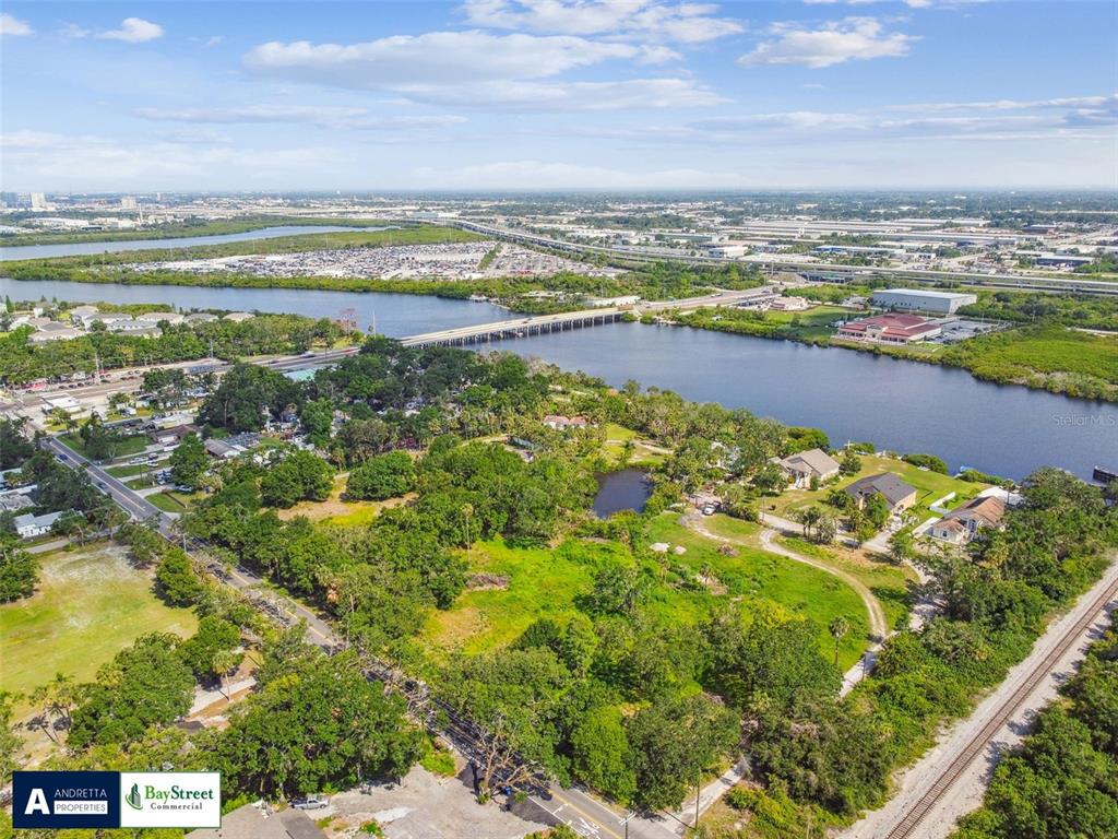An aerial view shows a large, grassy, tree-filled lot bordering a river and bridge — 5116 PALM RIVER ROAD, TAMPA, FL