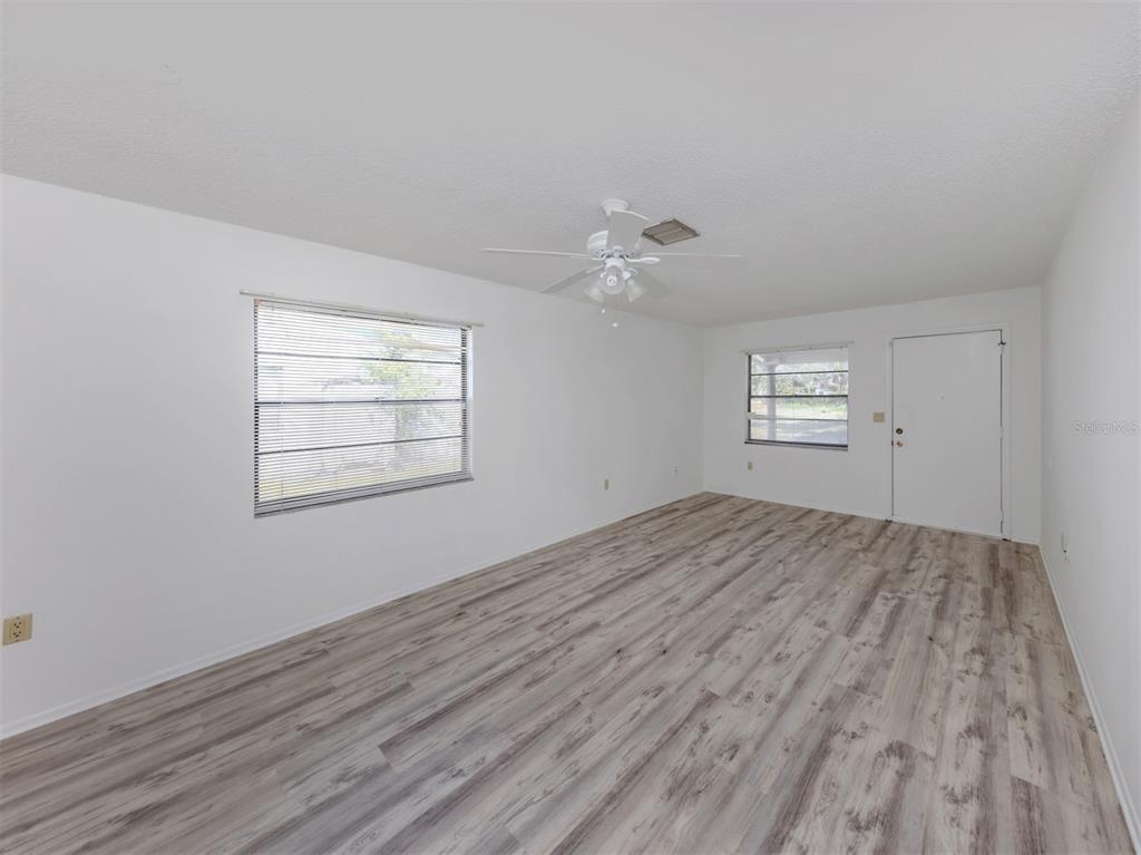 An empty room features white walls, light wood-look flooring, a ceiling fan, and two windows — 668 SUBSTATION ROAD, VENICE, FL