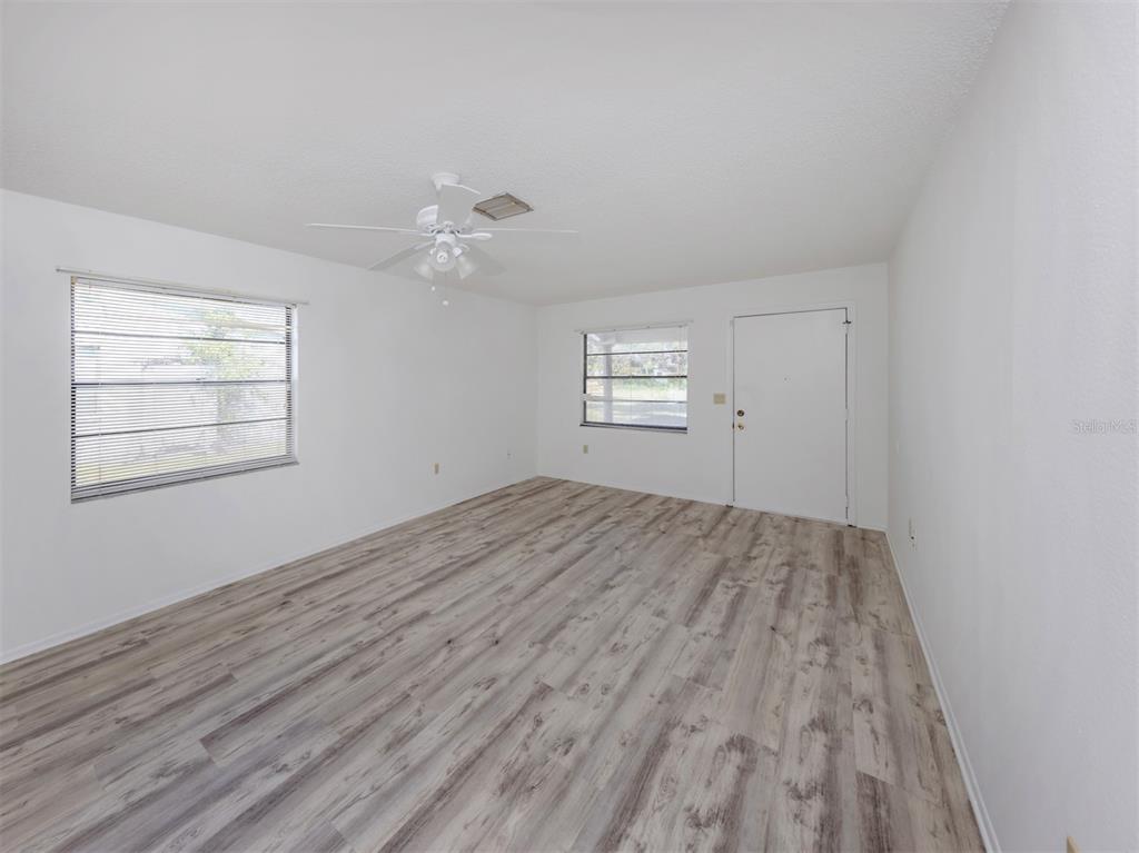 An empty room features white walls, light wood-look flooring, a ceiling fan, and two windows — 668 SUBSTATION ROAD, VENICE, FL