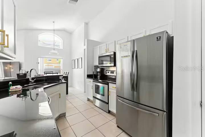 A kitchen with white cabinets, stainless steel appliances, and black countertops on a tiled floor — 1017 LAKE BERKLEY DR, KISSIMMEE, FL