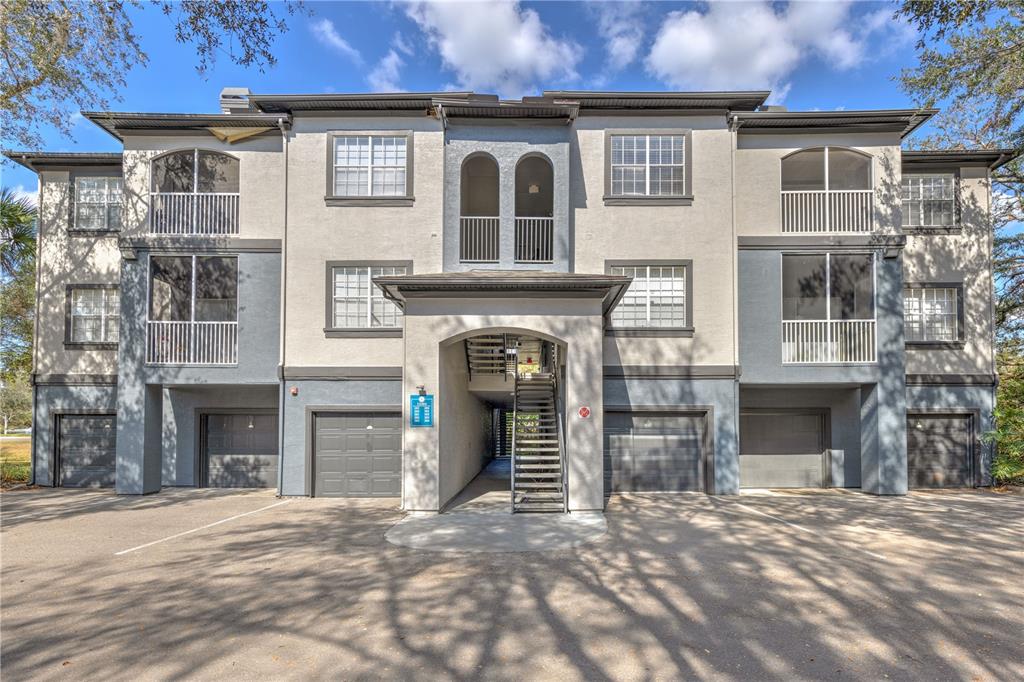 A three-story apartment building features ground-level garages, screened balconies, and a central outdoor staircase — 13304 SANCTUARY COVE DRIVE UNIT 303, TAMPA, FL