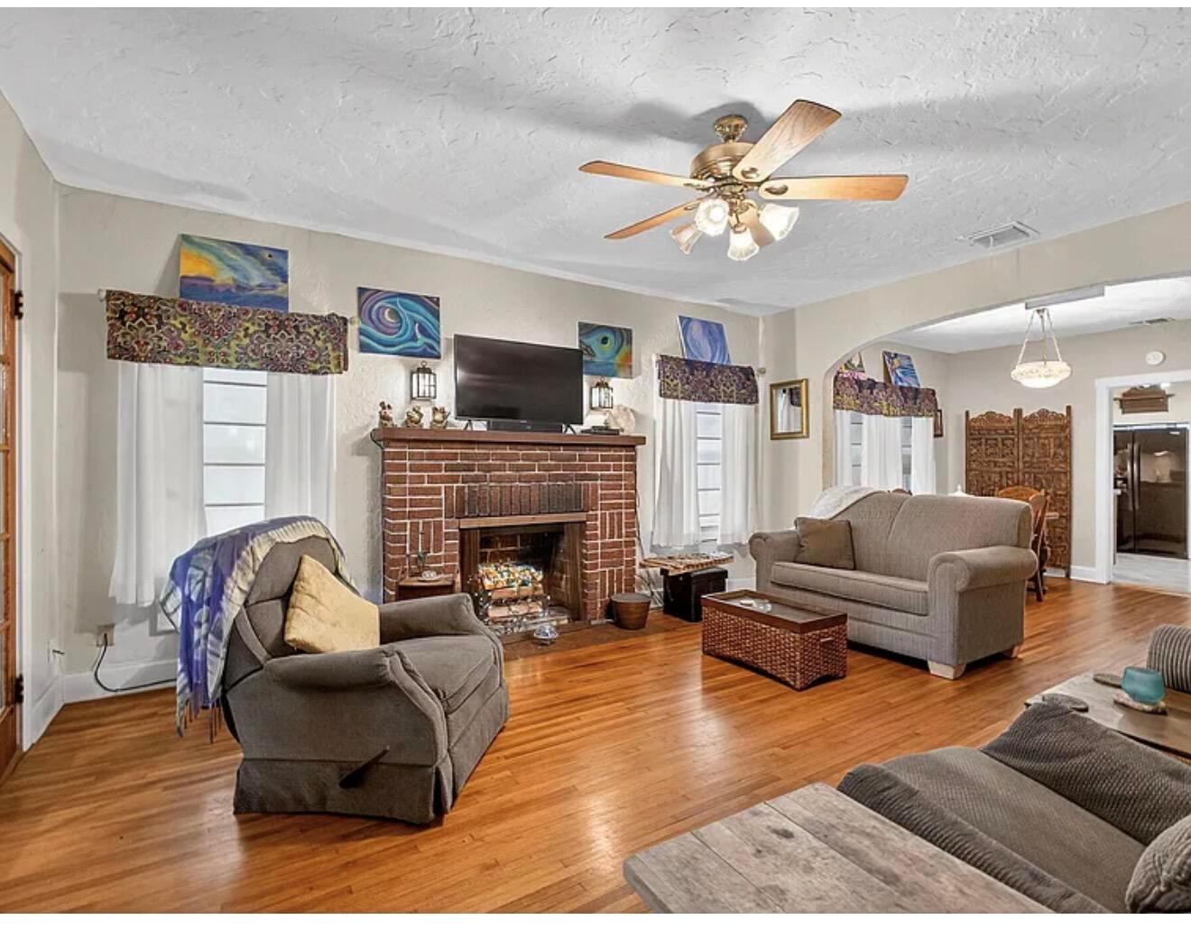 A living room with hardwood floors, a brick fireplace, and a ceiling fan — 705 Lytle Street, West Palm Beach FL 33405, WEST PALM BEACH, FL