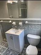 A bathroom features a white vanity, a toilet, a mirror, and gray tiled walls — 981 ARAGON AVENUE, WINTER PARK, FL