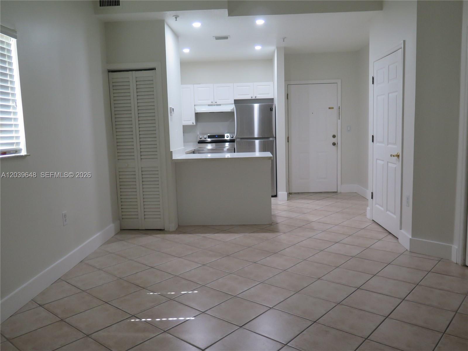 A kitchen with white cabinets and stainless steel appliances overlooks a tiled living area — 1918 Brickell Ave # 101, Miami FL 33129, MIAMI, FL