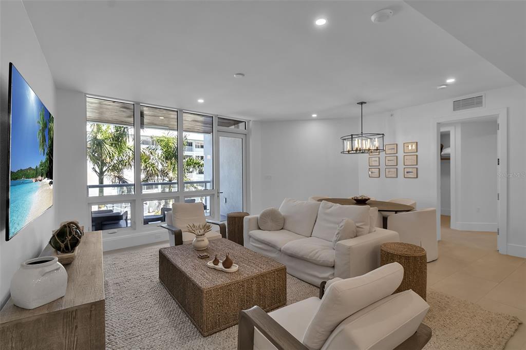 A bright living and dining area features white walls, a woven coffee table, and floor-to-ceiling windows — 1035 SEASIDE DRIVE UNIT 308, SARASOTA, FL