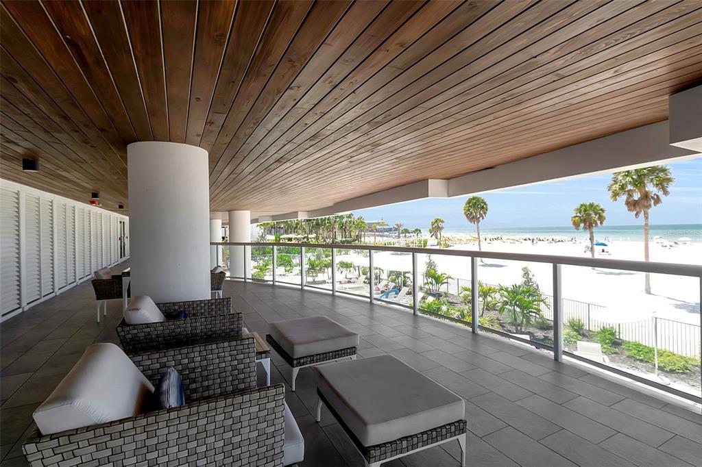 A covered balcony with wood-paneled ceilings, tiled floors, and outdoor seating overlooking a sandy beach — 1035 SEASIDE DRIVE UNIT 308, SARASOTA, FL