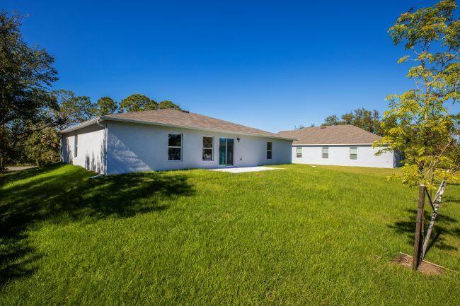 The back exterior of a light-colored house features a sliding glass door and a small patio — 462 Hazel Street, Sebastian FL 32958, SEBASTIAN, FL