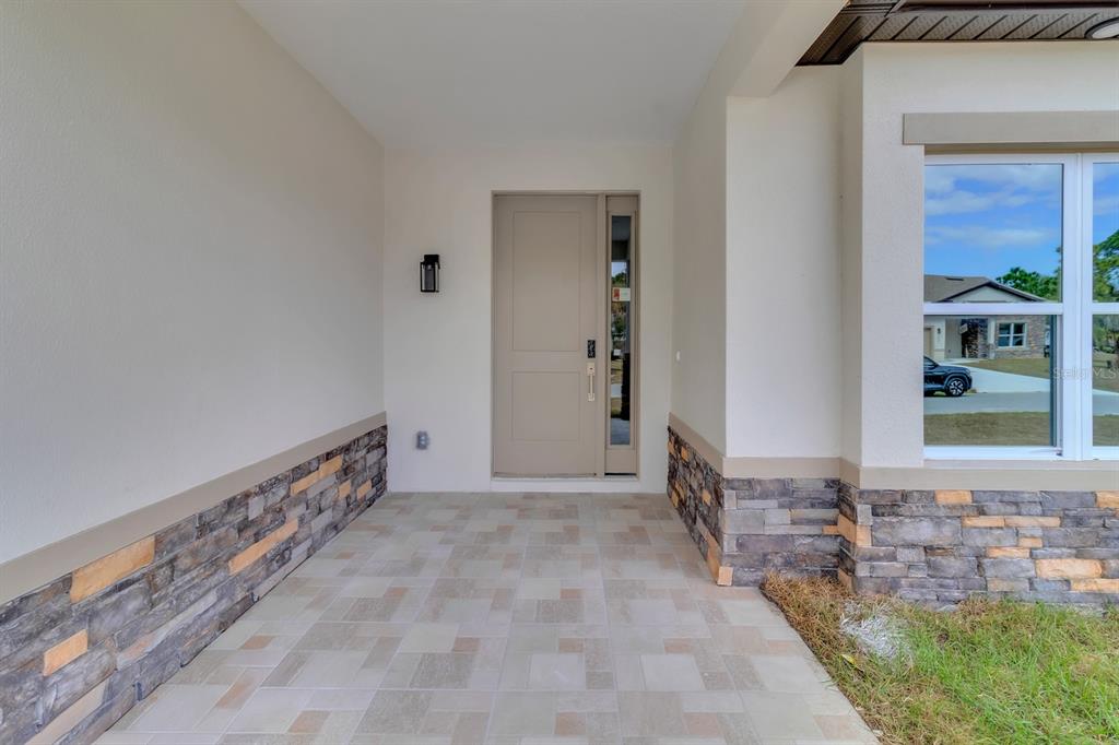 A covered entryway features a tan front door, stone veneer siding, and tiled flooring — 1821 MISSOURI ROAD NW, PALM BAY, FL