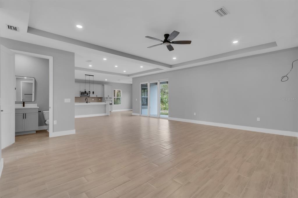 An open-concept living area features light wood-look tile flooring, a tray ceiling, and a kitchen — 1821 MISSOURI ROAD NW, PALM BAY, FL
