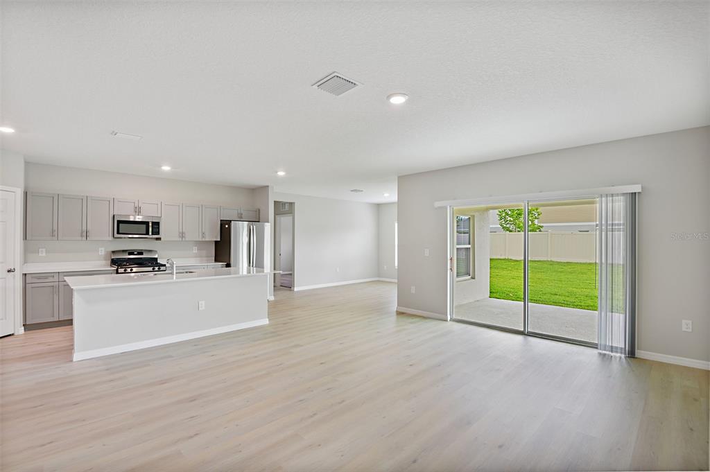 An open-concept kitchen and living area features light wood flooring, gray cabinets, and sliding doors — 31670 BARONNE STREET, WESLEY CHAPEL, FL