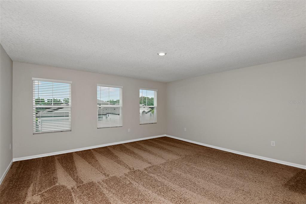 An empty room with beige walls, brown carpet, and three windows with white blinds — 31670 BARONNE STREET, WESLEY CHAPEL, FL