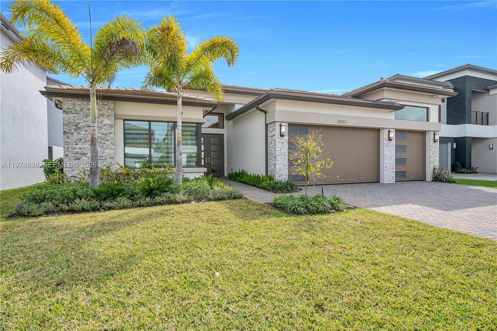 A modern single-story house features a stone facade, two garage doors, and a paved driveway — 20052 Pacific Dunes Dr, Boca Raton FL 33434, BOCA RATON, FL