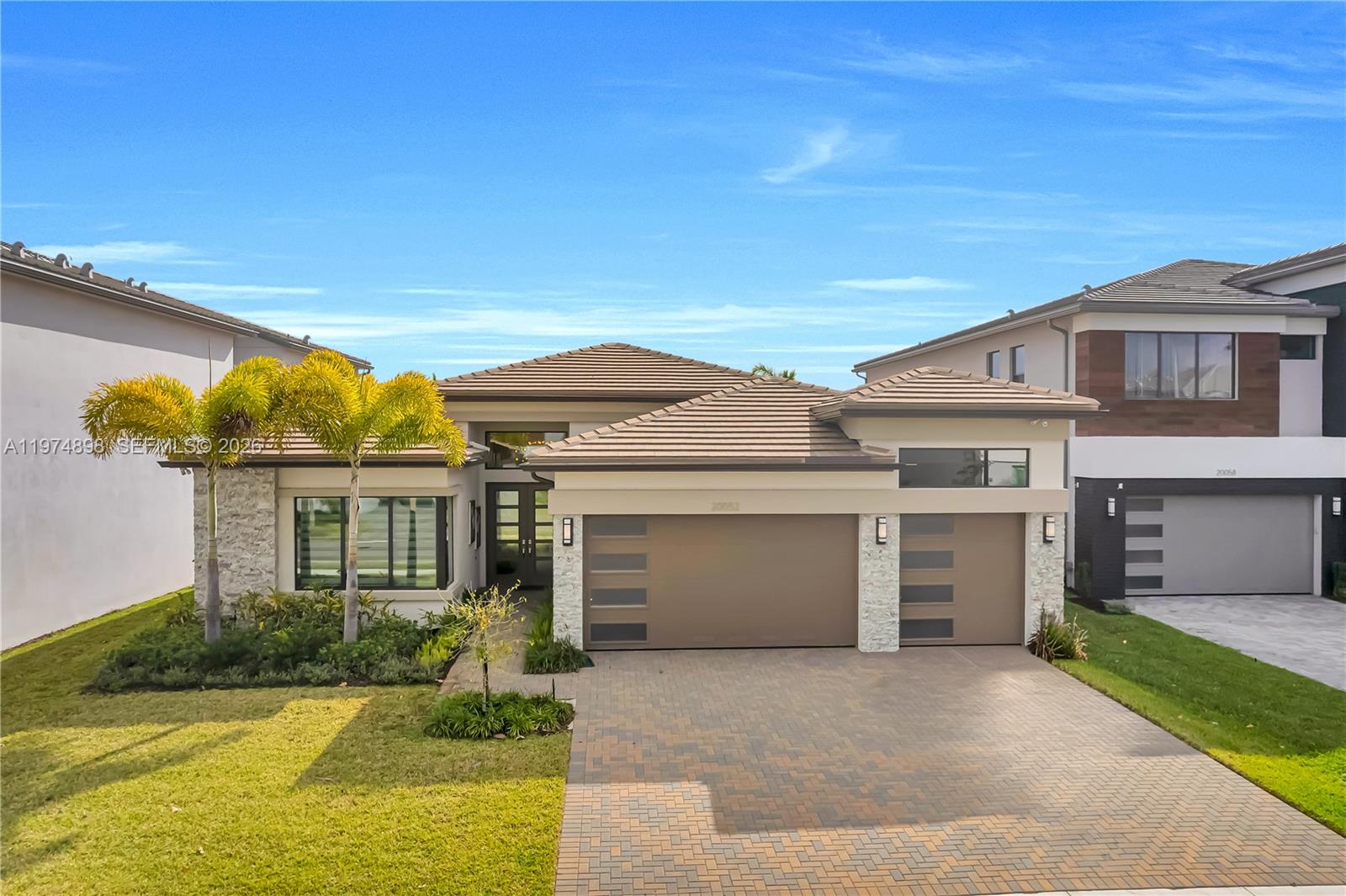 A modern single-story house features a stone facade, palm trees, and a paved driveway — 20052 Pacific Dunes Dr, Boca Raton FL 33434, BOCA RATON, FL