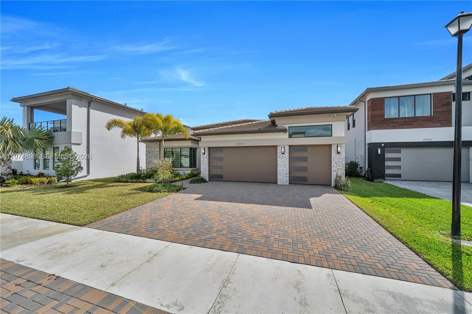 A modern single-story house features a three-car garage, stone accents, and palm trees — 20052 Pacific Dunes Dr, Boca Raton FL 33434, BOCA RATON, FL