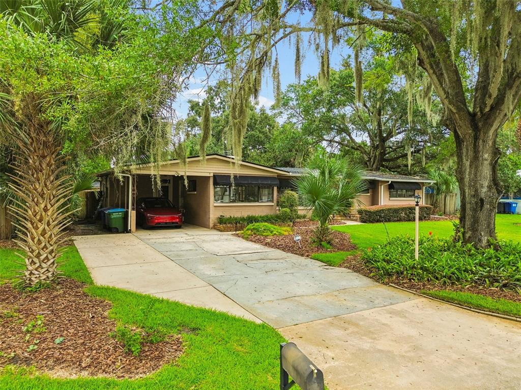 A single-story brick house with a carport, concrete driveway, and large trees in the yard — 228 RIPPLING LANE, WINTER PARK, FL
