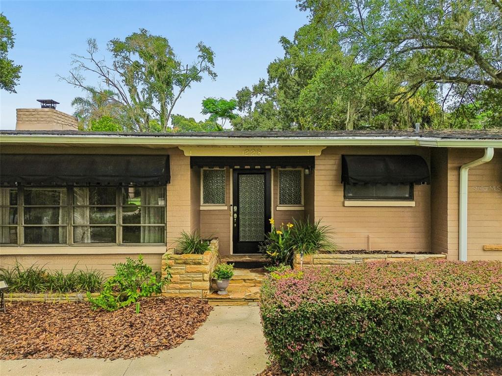 A single-story brick house features a front entrance with stone planters and black window awnings — 228 RIPPLING LANE, WINTER PARK, FL