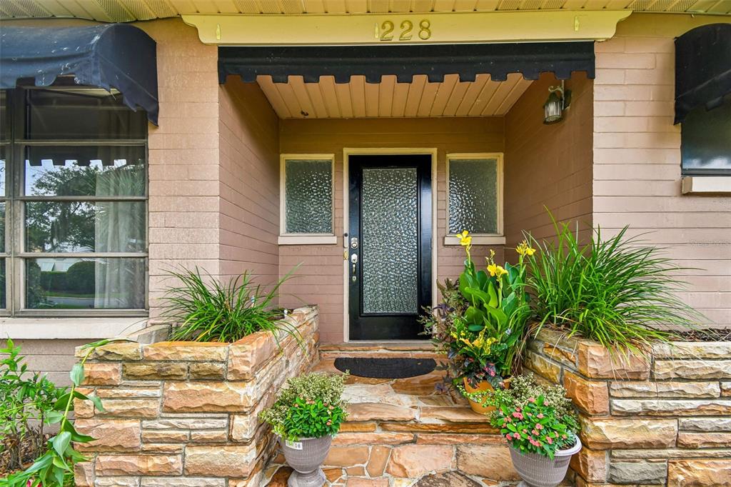The front entrance features a black door, stone planters, and a tan brick exterior — 228 RIPPLING LANE, WINTER PARK, FL