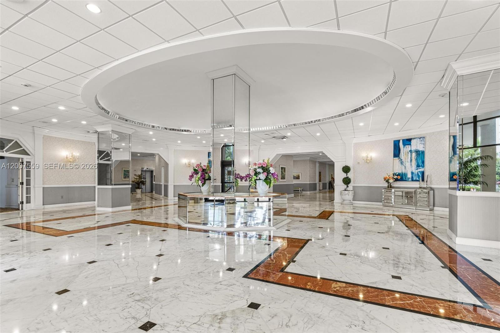 A spacious lobby features white marble floors with brown accents, a mirrored central pillar, and recessed lighting — 3800 S Ocean Dr # 301, Hollywood FL 33019, HOLLYWOOD, FL