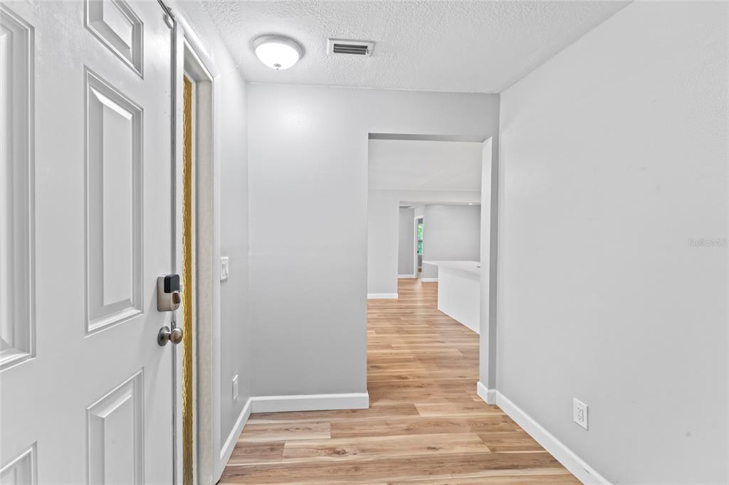 An entryway with light wood-look flooring leads into an open-concept living area with white walls — 1127 WYATT STREET N, CLEARWATER, FL