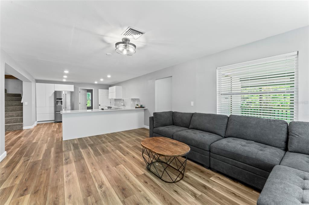 A living room with wood-look flooring and a large gray sectional faces an open kitchen — 1127 WYATT STREET N, CLEARWATER, FL
