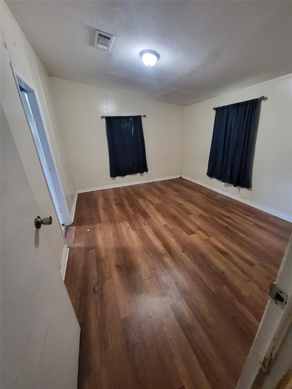An empty room features wood-look flooring, white walls, two windows with dark curtains, and a ceiling light — 36639 KEEUKA ROAD, ZEPHYRHILLS, FL
