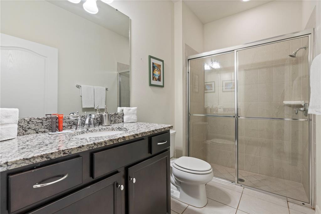 A bathroom features a dark wood vanity with a granite countertop, toilet, and glass-enclosed shower — 2428 DUBAI STREET, KISSIMMEE, FL