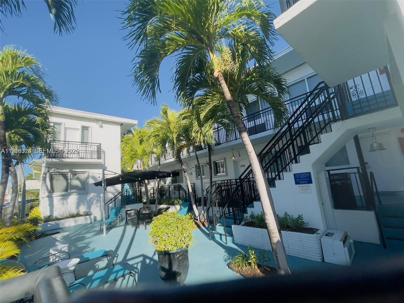 An outdoor courtyard features palm trees, a patio seating area, and stairs leading to upper units — 8100 Harding Ave # 513, Miami Beach FL 33141, MIAMI BEACH, FL