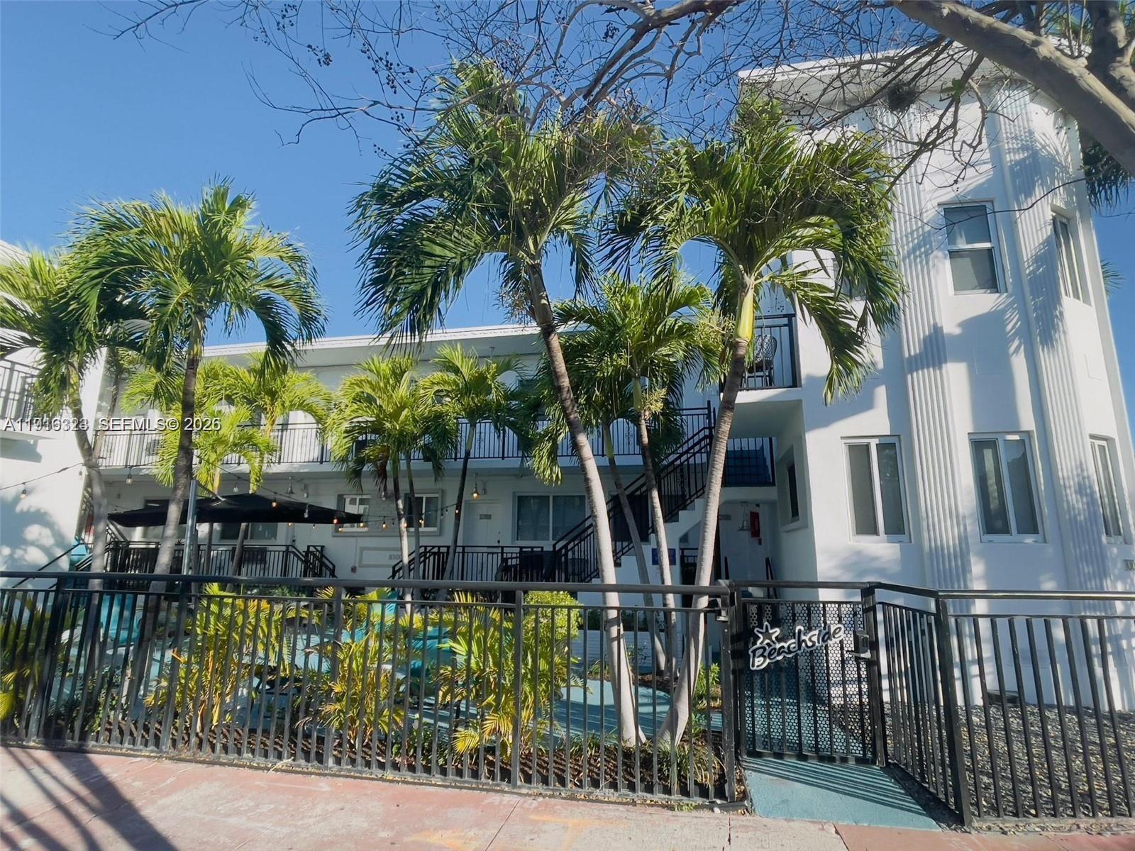 A white multi-story apartment building features palm trees and a gated entrance with signage — 8100 Harding Ave # 513, Miami Beach FL 33141, MIAMI BEACH, FL
