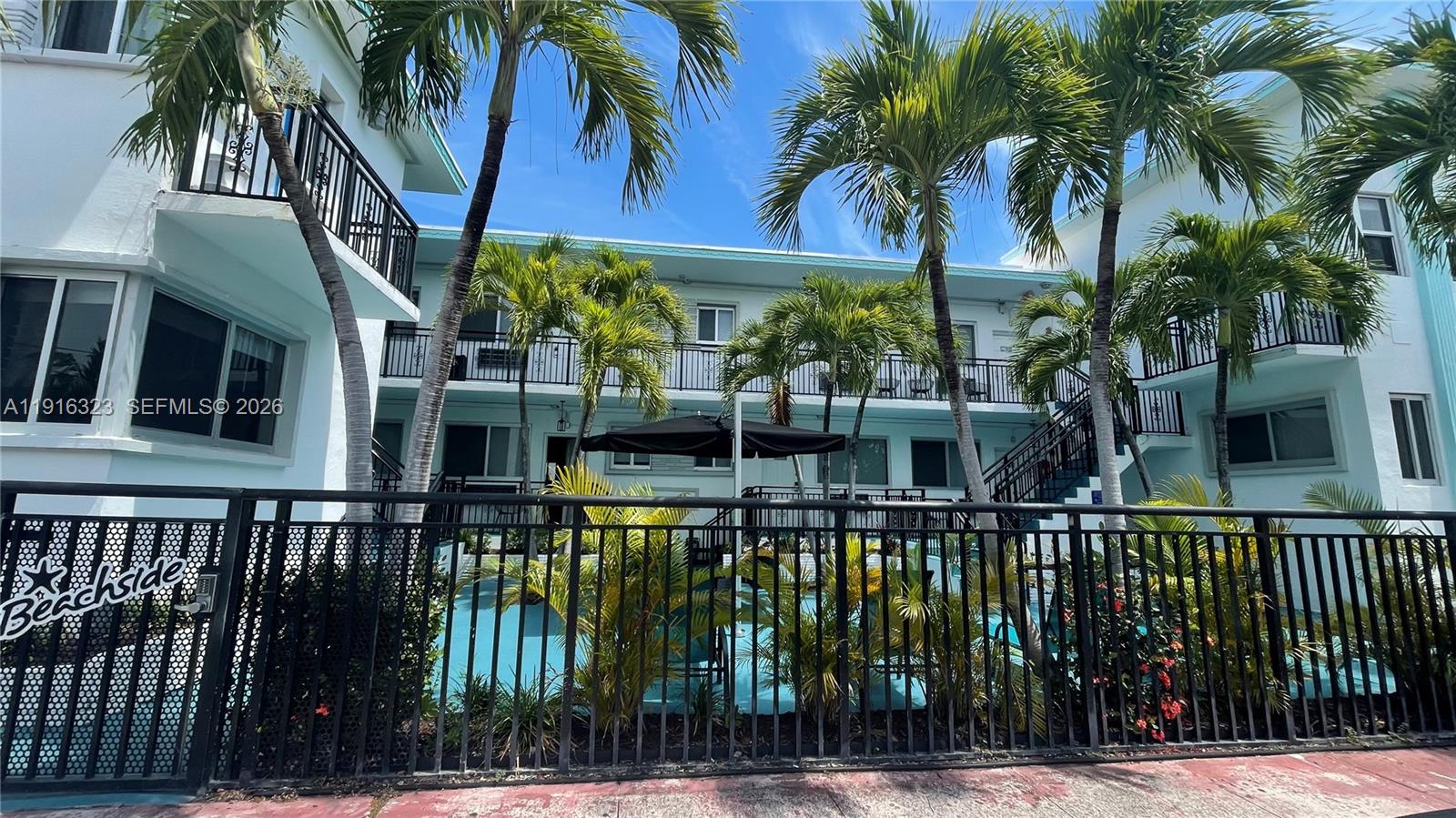 A black metal fence surrounds a swimming pool area in front of a multi-story building — 8100 Harding Ave # 513, Miami Beach FL 33141, MIAMI BEACH, FL