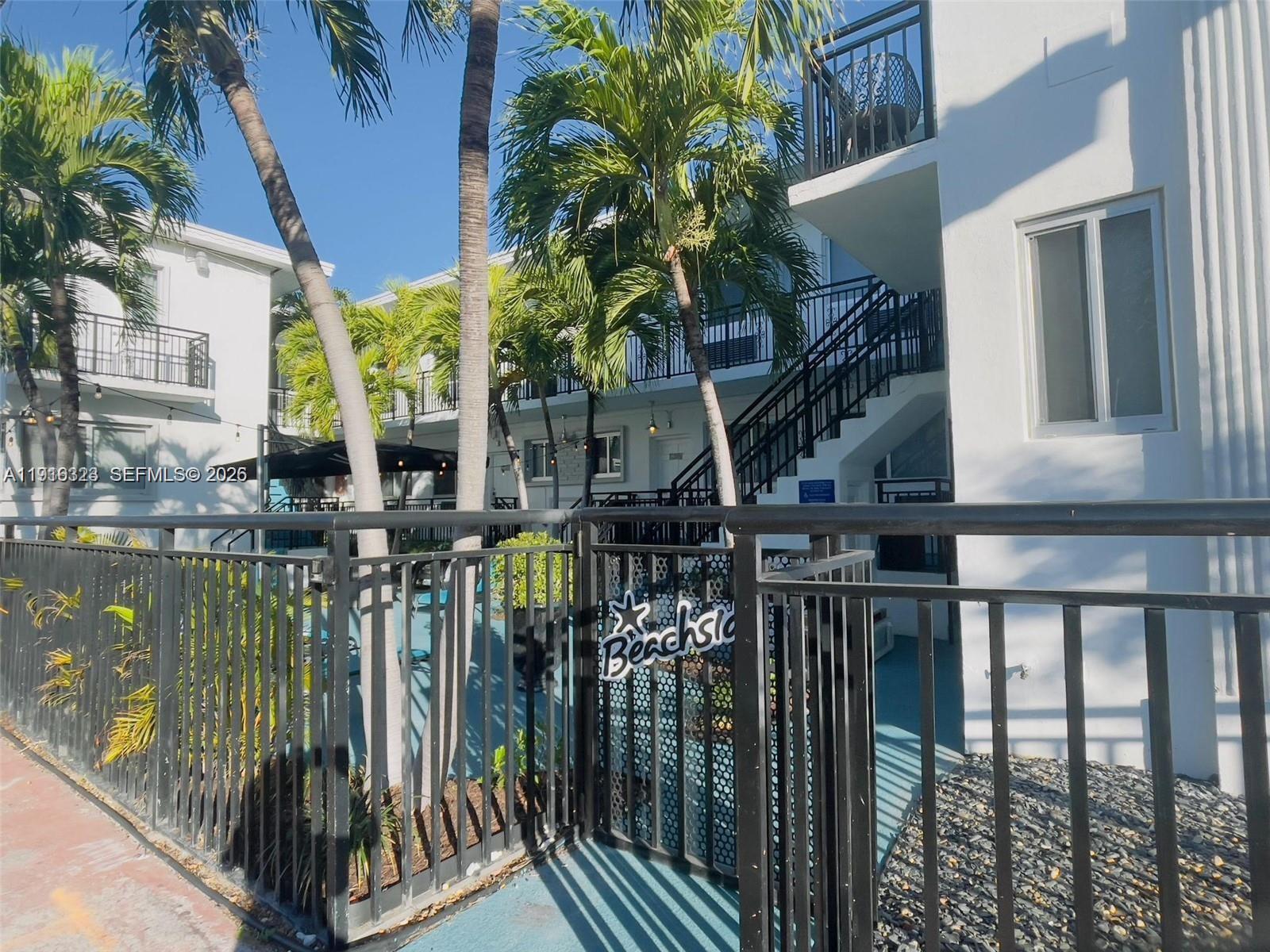 A black metal fence surrounds a courtyard with palm trees and a multi-story building — 8100 Harding Ave # 513, Miami Beach FL 33141, MIAMI BEACH, FL