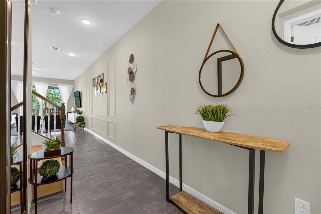 A hallway features gray tile flooring, a wood-topped console table, and decorative wall molding — 1555 CAREY PALM CIRCLE, KISSIMMEE, FL