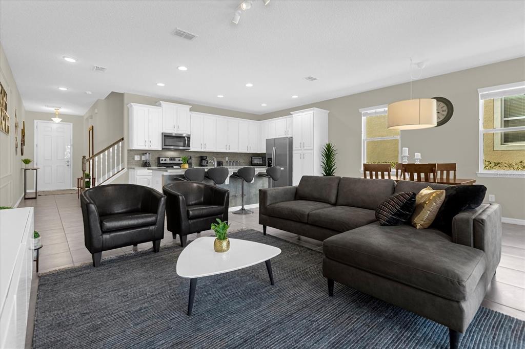 An open-concept living room and kitchen featuring white cabinetry, dark furniture, and a gray rug — 1555 CAREY PALM CIRCLE, KISSIMMEE, FL