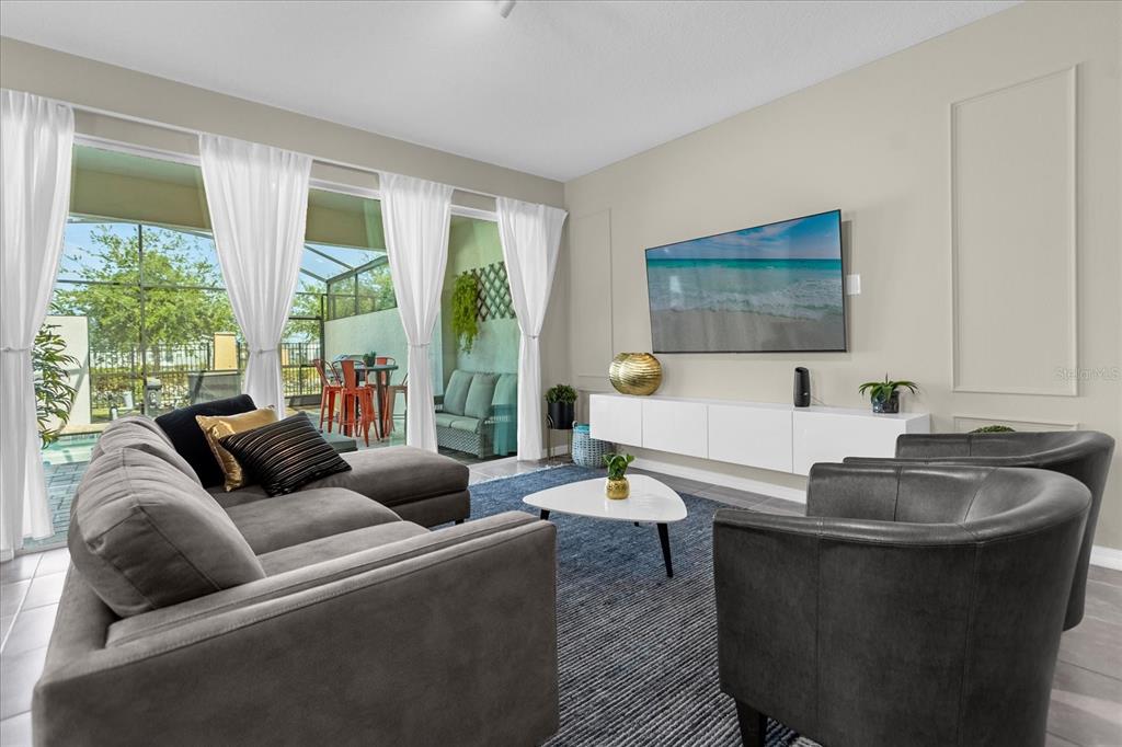 A living room features a grey sectional, two armchairs, a white media console, and patio access — 1555 CAREY PALM CIRCLE, KISSIMMEE, FL